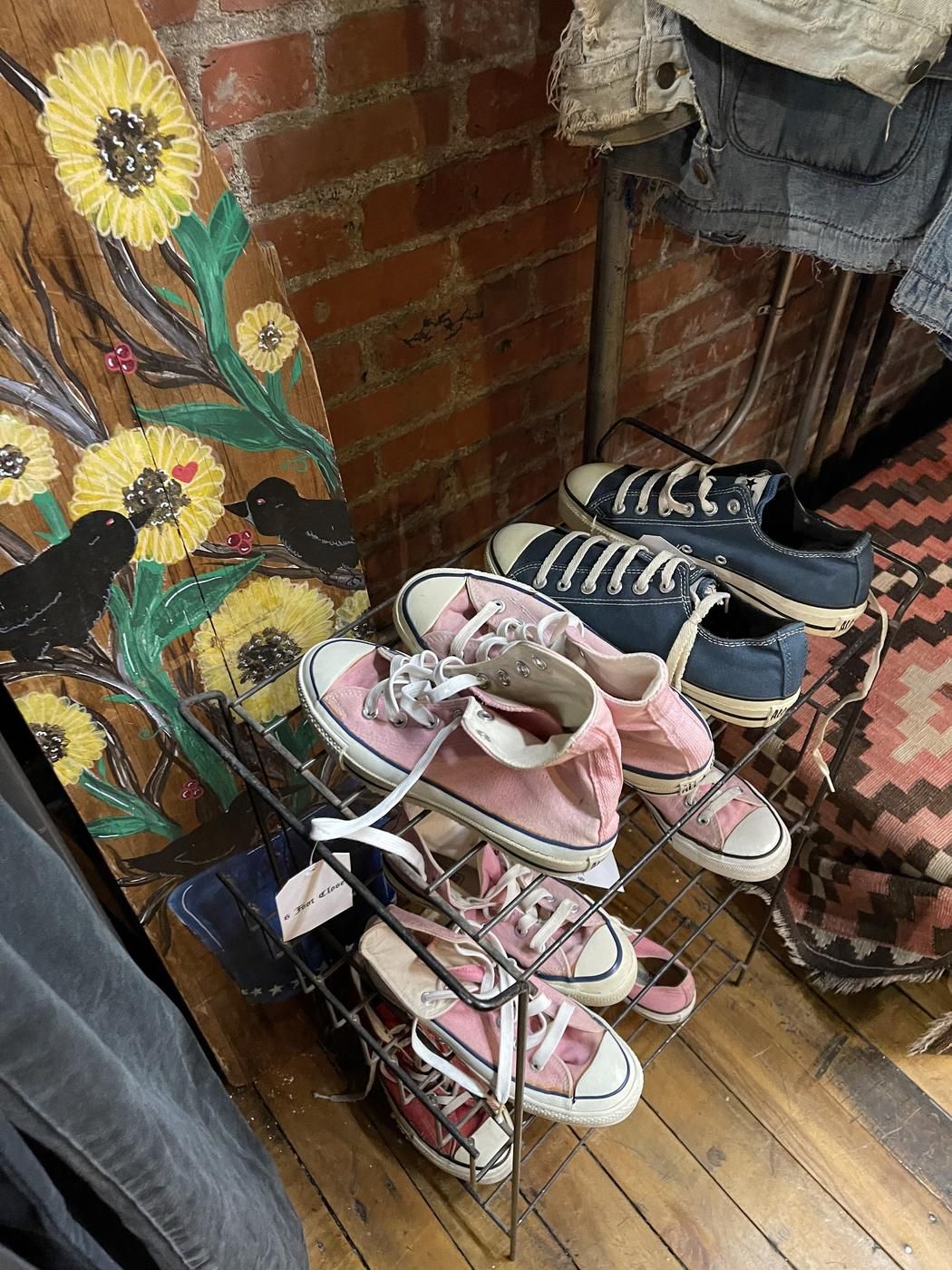 Pink and navy canvas sneakers on a wire rack beside a hand painted folk art board