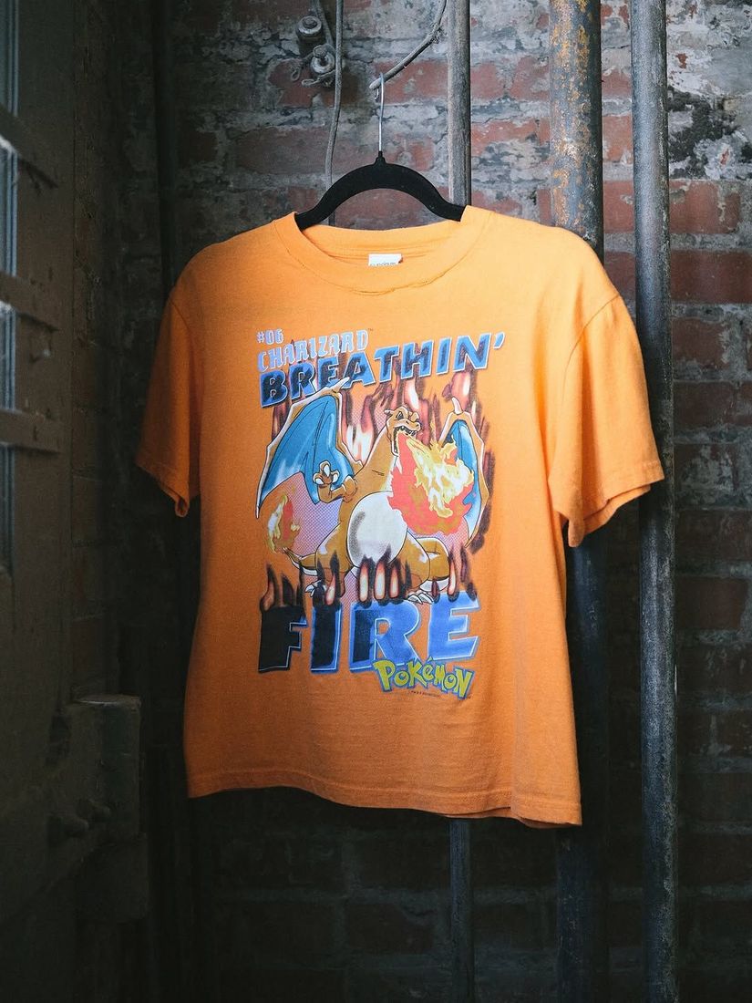A vintage Charizard tee shirt on a hanger against the painted brick wall at 6 Foot Closet